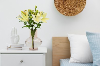 Vase with bouquet of fresh flowers on nightstand in bedroom