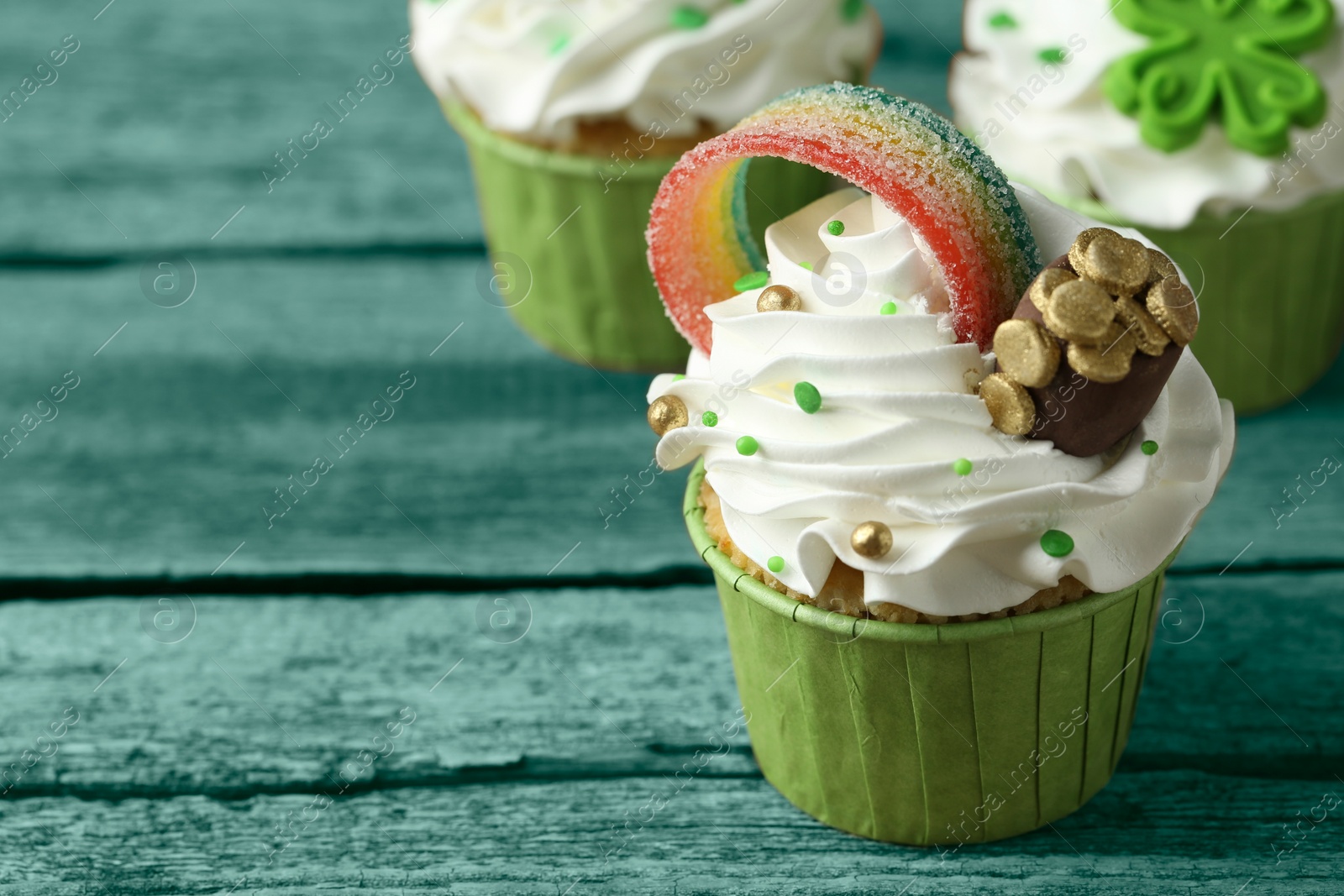 Image of St. Patrick's day. Tasty festively decorated cupcakes on green wooden table, closeup. Space for text