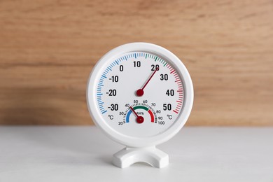 Photo of Round hygrometer with thermometer on white table, closeup