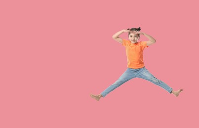 Cute girl jumping on pink background, space for text