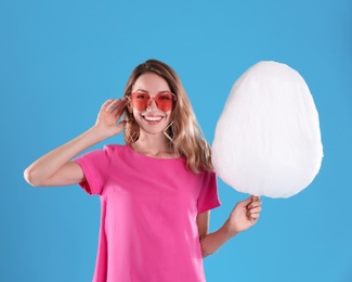 Happy young woman with cotton candy on blue background