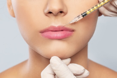 Young woman getting lips injection on grey background, closeup. Cosmetic surgery