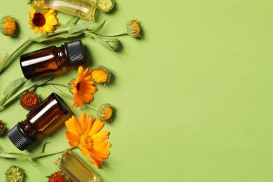 Bottles of essential oils and beautiful calendula flowers on green background, flat lay. Space for text