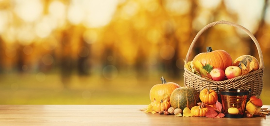 Image of Happy Thanksgiving day. Fresh pumpkins, acorns, apples, walnuts and fallen leaves on wooden table outdoors, space for text 