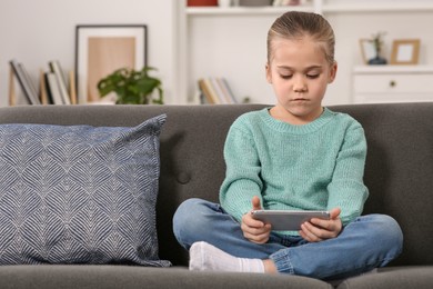 Little girl using smartphone on sofa at home. Internet addiction
