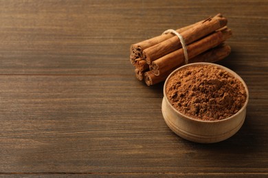 Aromatic cinnamon powder and sticks on wooden table, space for text