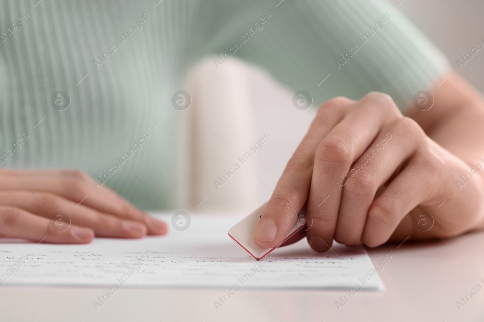 Photo of Girl erasing mistake in her notebook at white desk, closeup