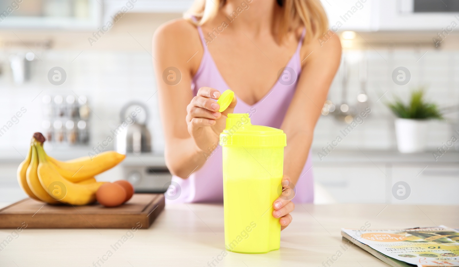 Photo of Young woman opening bottle of protein shake at table with ingredients, closeup