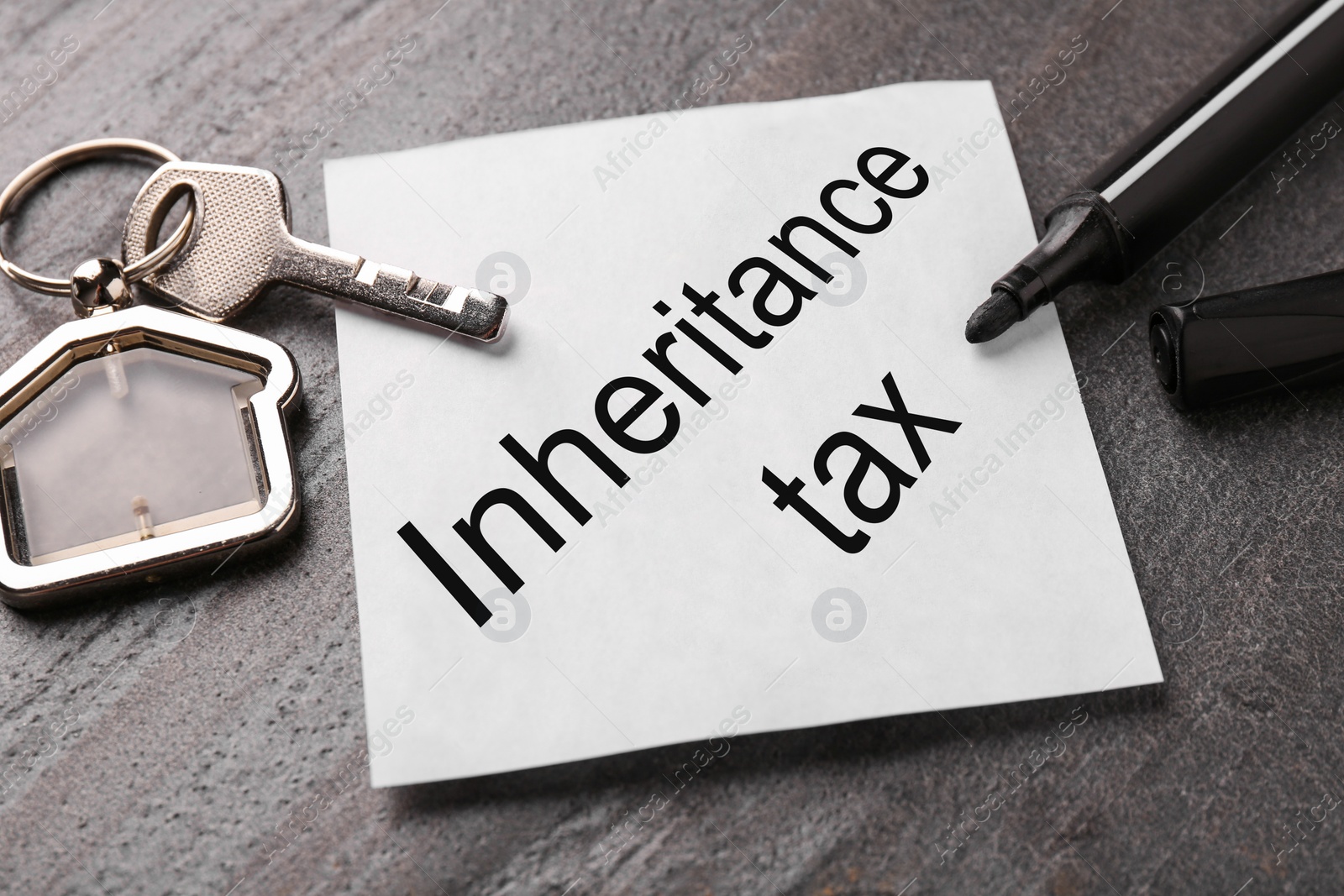 Photo of Inheritance Tax. Paper note, key with key chain in shape of house and marker on grey table, closeup