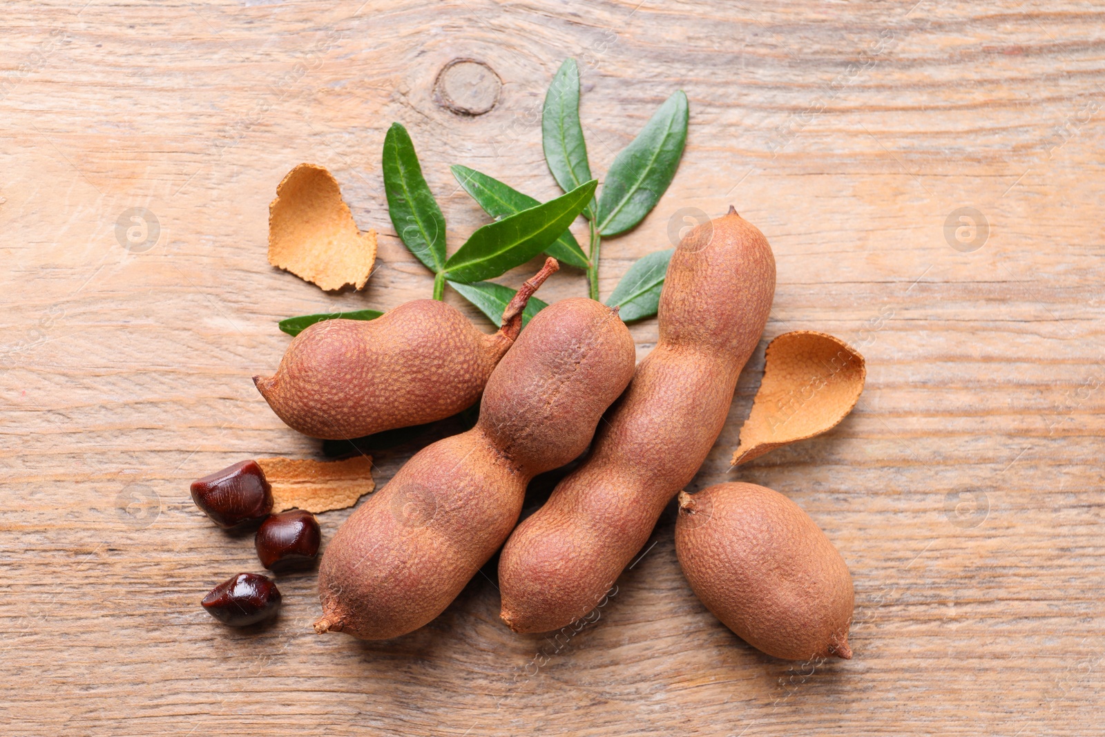 Photo of Ripe tamarinds and fresh leaves on wooden table, flat lay