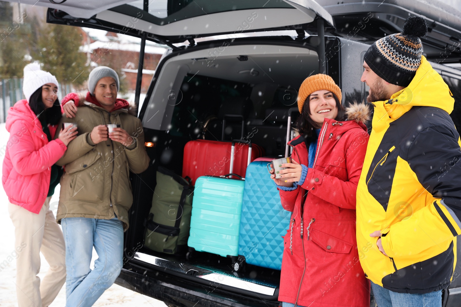 Photo of Group of friends near car with open trunk on snowy road. Winter vacation