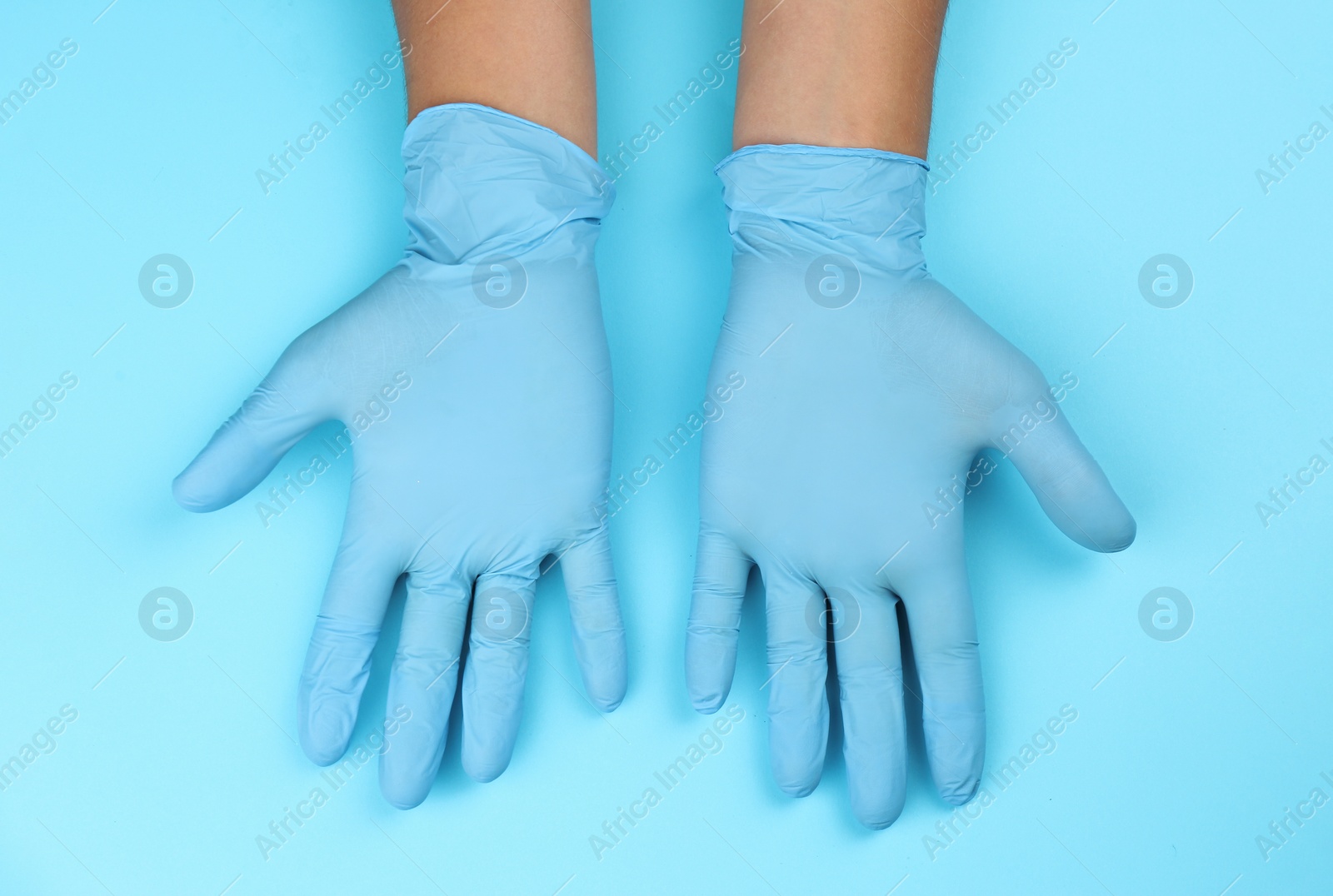 Photo of Person in latex gloves against light blue background, closeup on hands