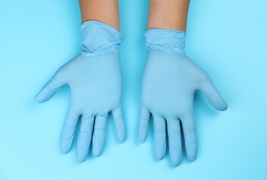 Person in latex gloves against light blue background, closeup on hands