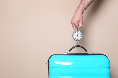 Photo of Man weighing stylish suitcase against color background, closeup. Space for text