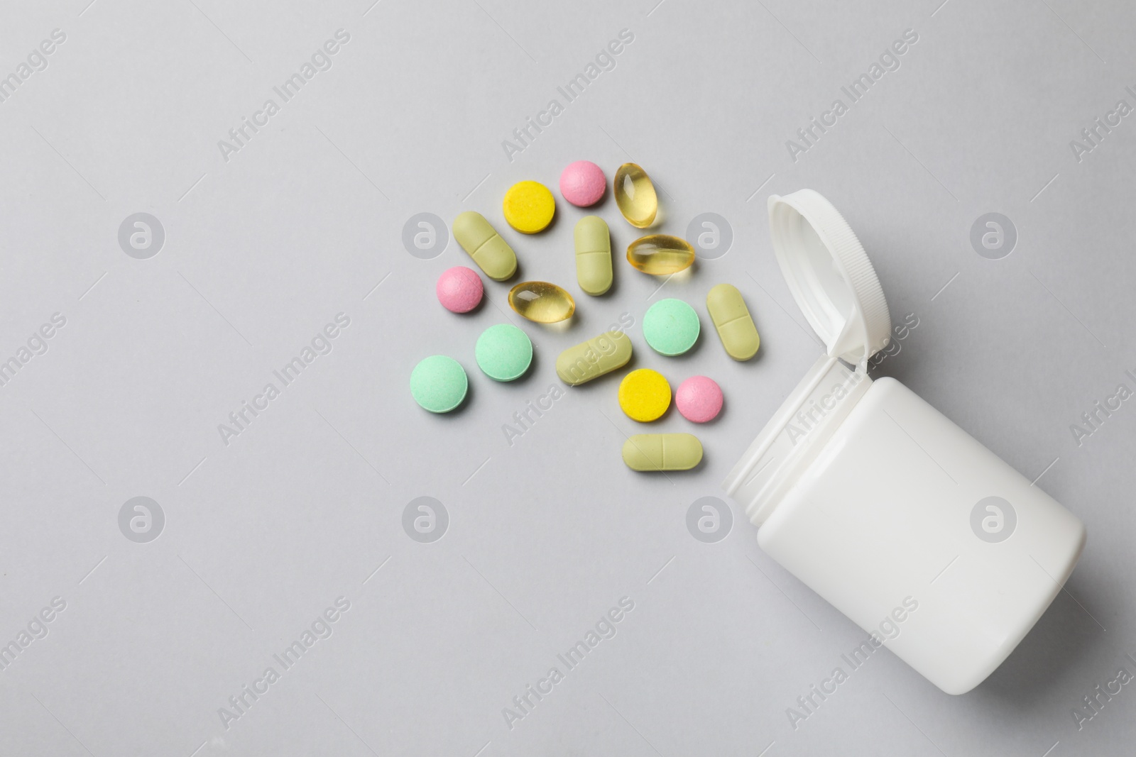 Photo of Different vitamin pills and bottle on grey background, top view. Space for text