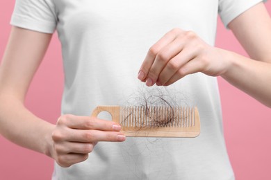 Photo of Woman untangling her lost hair from comb on pink background, closeup. Alopecia problem