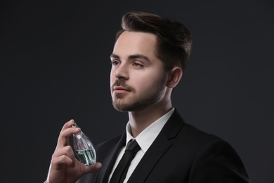 Photo of Handsome man in suit using perfume on dark background