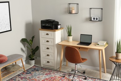 Photo of Stylish room interior with chest of drawers, modern printer and laptop