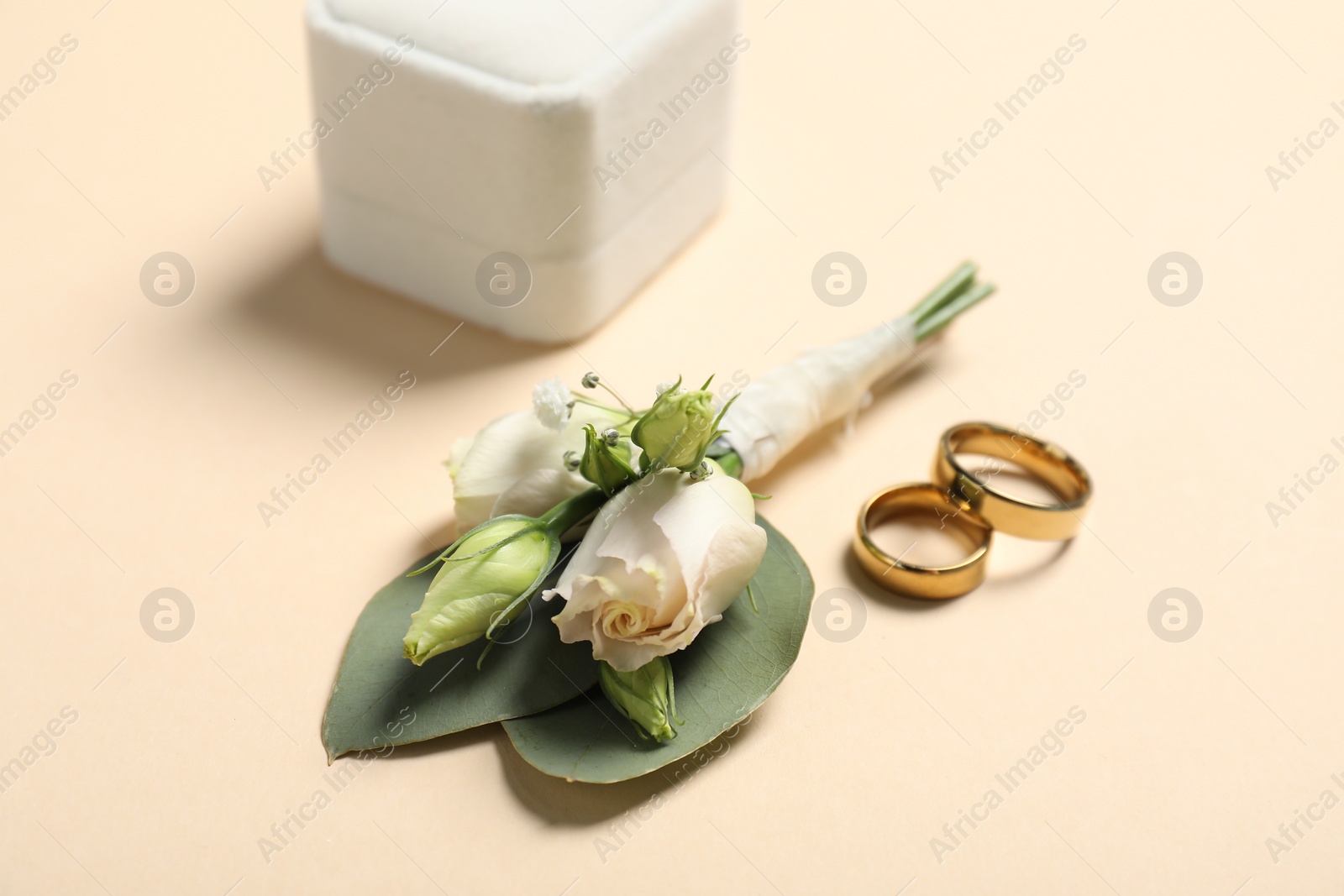 Photo of Wedding stuff. Stylish boutonniere and rings on beige background, closeup