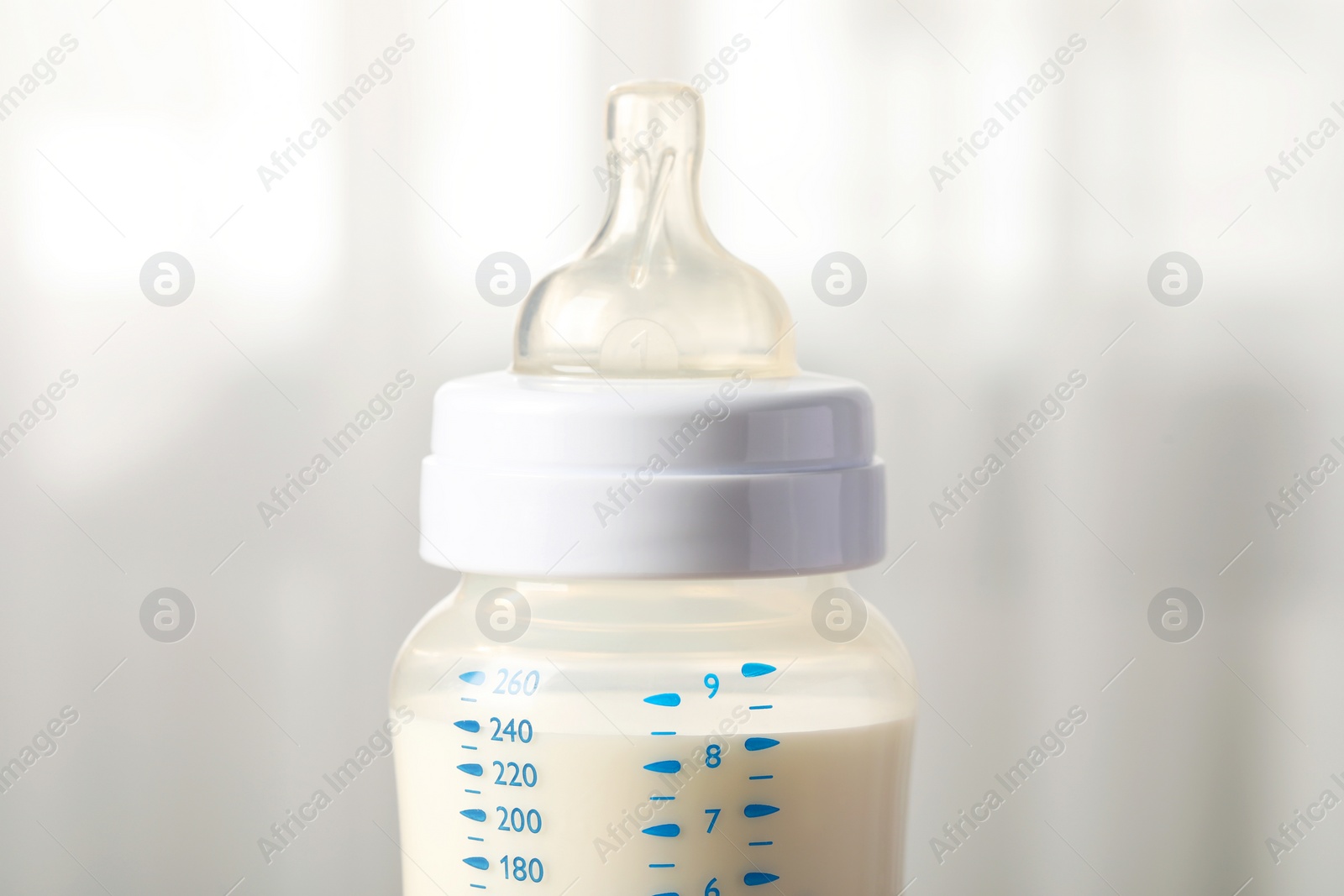 Photo of Feeding bottle with milk indoors, closeup view