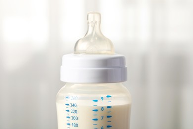 Feeding bottle with milk indoors, closeup view