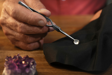 Photo of Professional jeweler working with beautiful gemstone at table, closeup