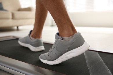 Photo of Sporty man training on walking treadmill at home, closeup