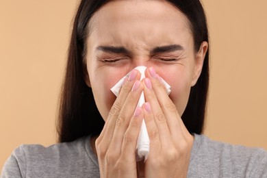 Photo of Suffering from allergy. Young woman blowing her nose in tissue on beige background, closeup