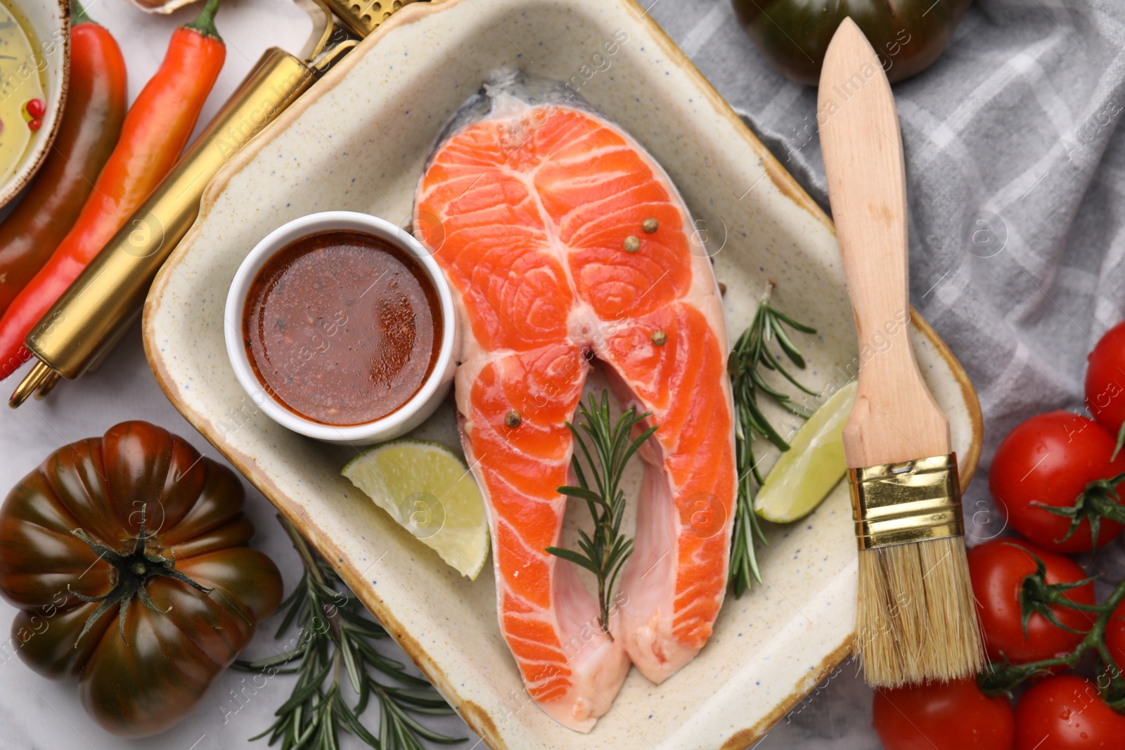 Photo of Fresh fish, lime, rosemary and marinade in baking dish surrounded by products on light table, flat lay