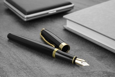 Stylish black fountain pen, notebook and cigarette case on grey textured table, closeup