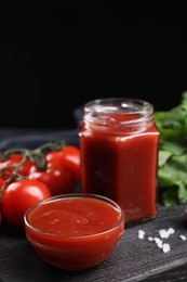Photo of Delicious ketchup on black wooden table, closeup. Tomato sauce