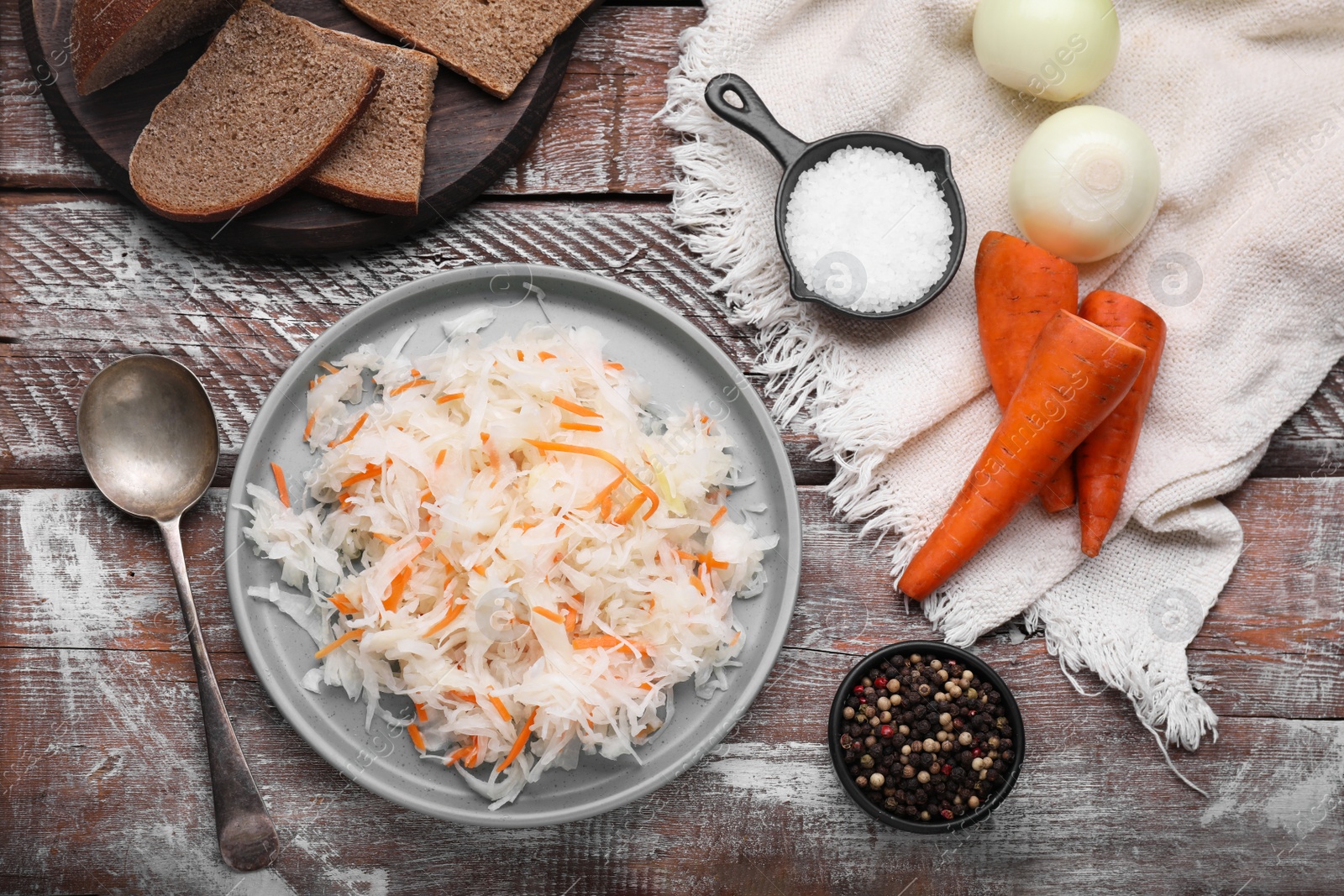 Photo of Bowl of tasty sauerkraut and ingredients on wooden table, flat lay