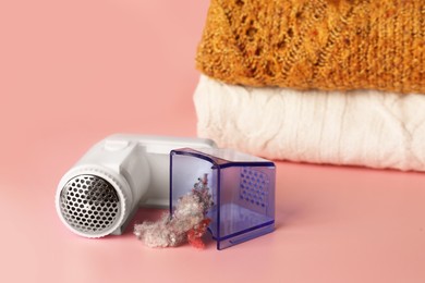 Modern fabric shaver with fuzz and knitted clothes on pink background, space for text