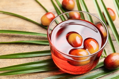 Palm oil in glass with fruits and tropical leaf on wooden table, closeup