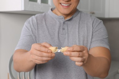 Photo of Happy man holding tasty fortune cookie with prediction indoors, closeup