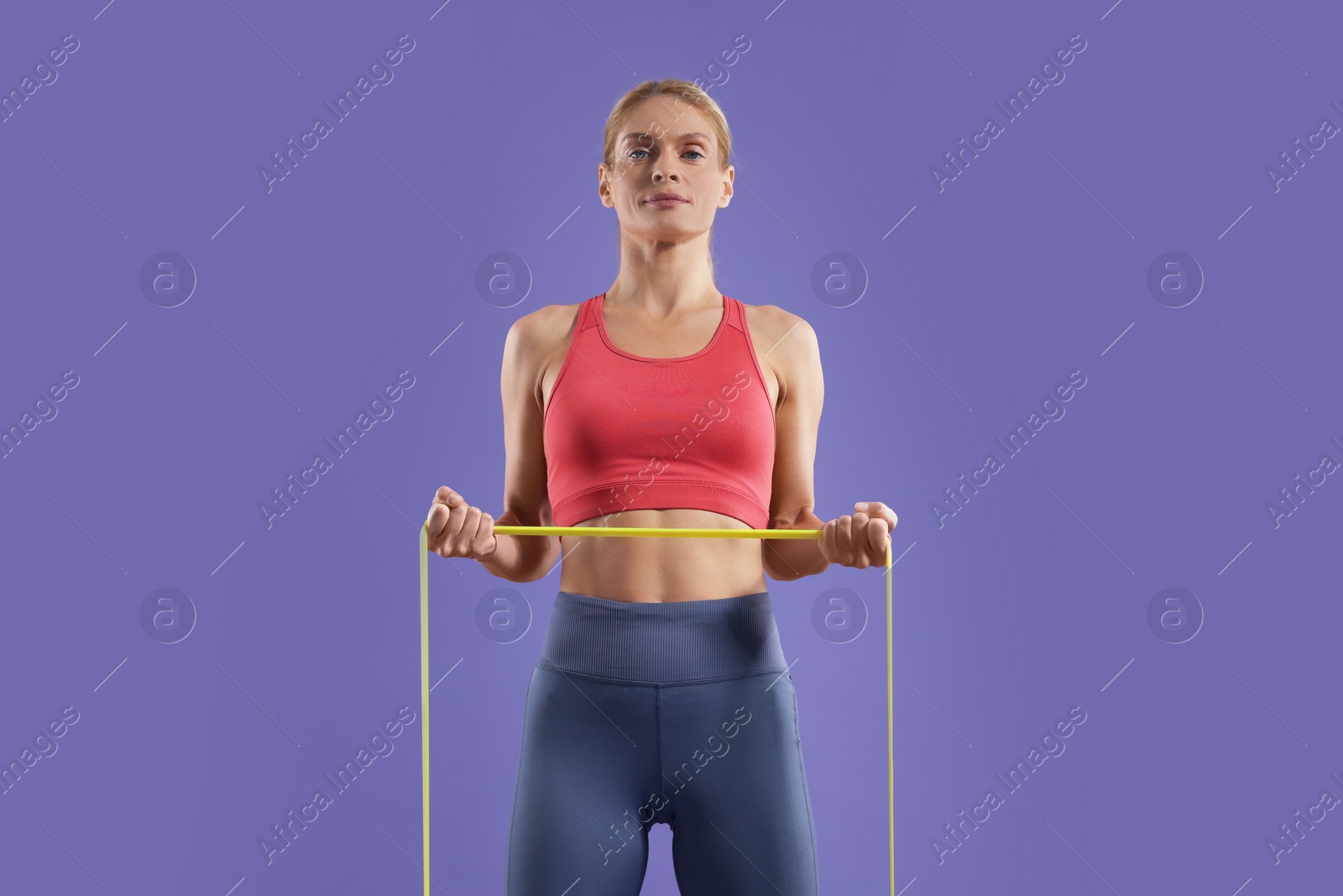 Photo of Athletic woman exercising with elastic resistance band on purple background, low angle view