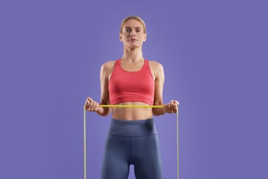 Photo of Athletic woman exercising with elastic resistance band on purple background, low angle view