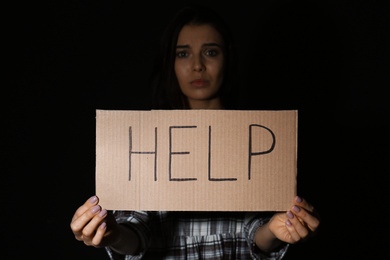 Photo of Abused young woman with sign HELP on black background. Domestic violence concept
