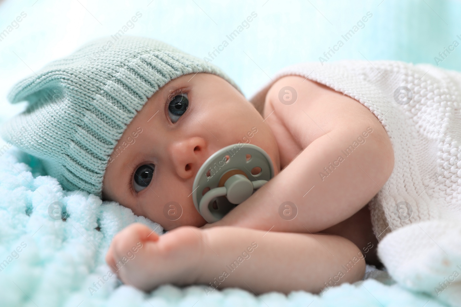 Photo of Cute newborn baby with pacifier on light blue blanket, closeup