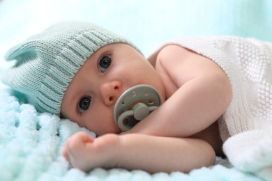 Photo of Cute newborn baby with pacifier on light blue blanket, closeup