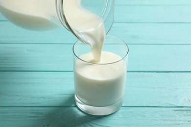 Pouring milk into glass on light blue wooden table