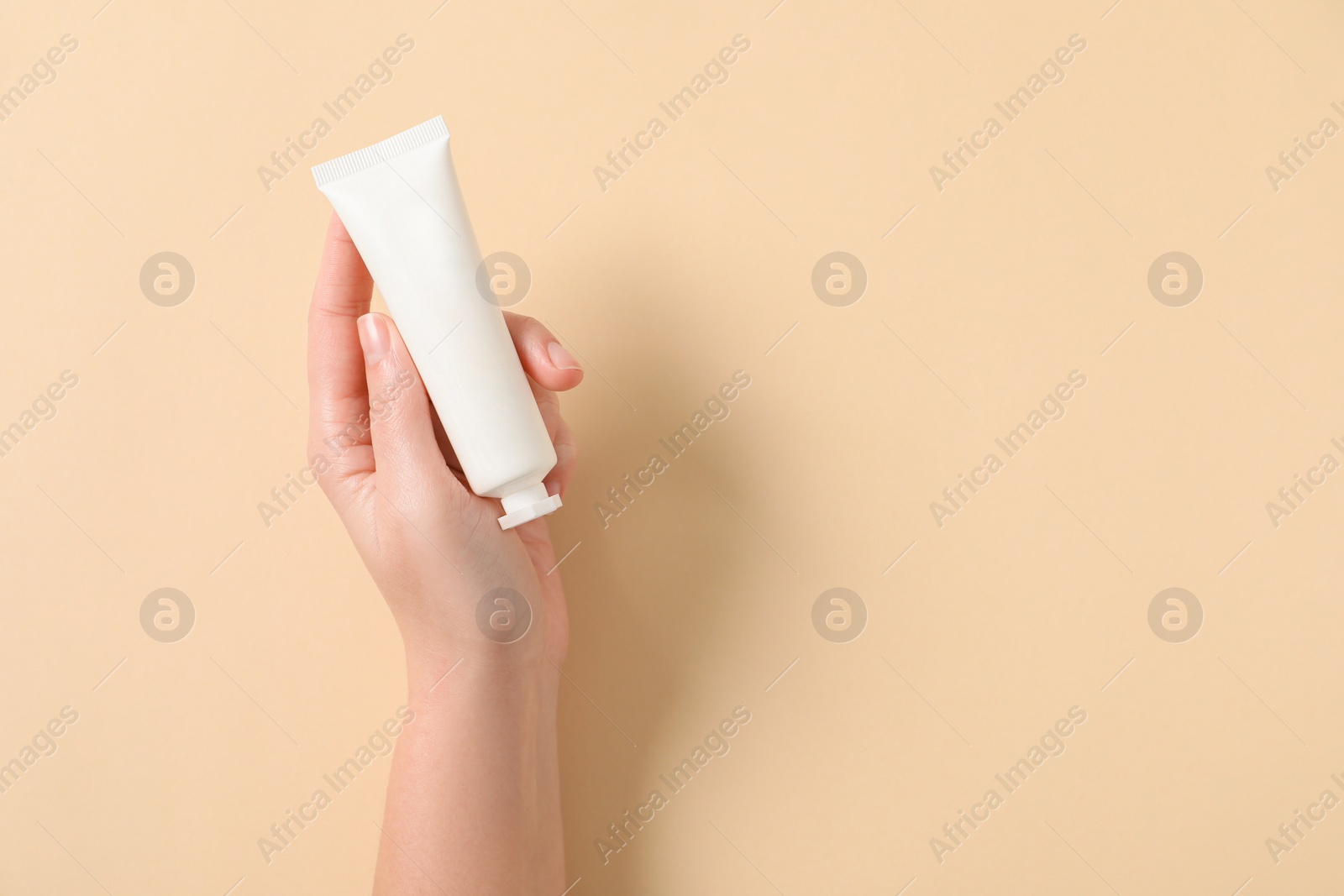 Photo of Woman with tube of hand cream on beige background, top view. Space for text