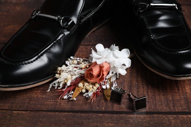 Photo of Wedding stuff. Stylish boutonniere and black shoes on wooden background, closeup