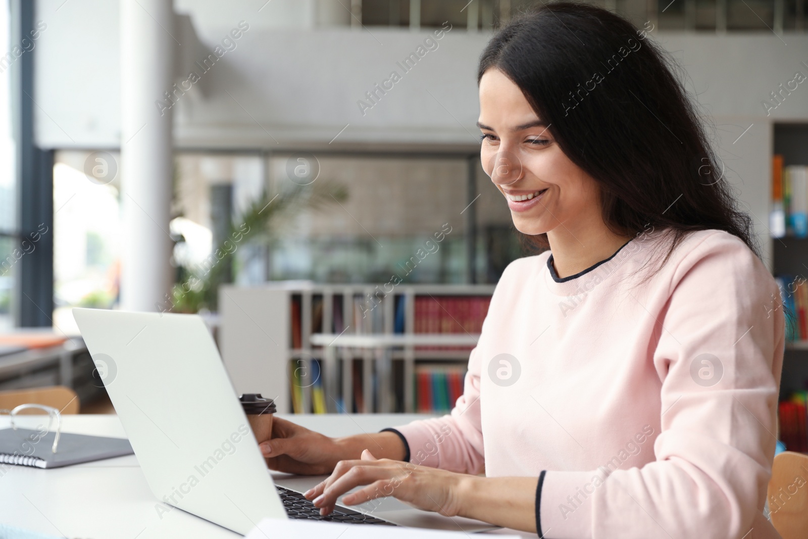 Photo of Young happy woman using laptop at table in library