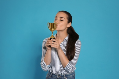 Photo of Portrait of happy young woman kissing gold trophy cup on blue background