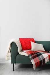 Photo of Sofa with soft pillows and warm plaids near light wall indoors. Space for text