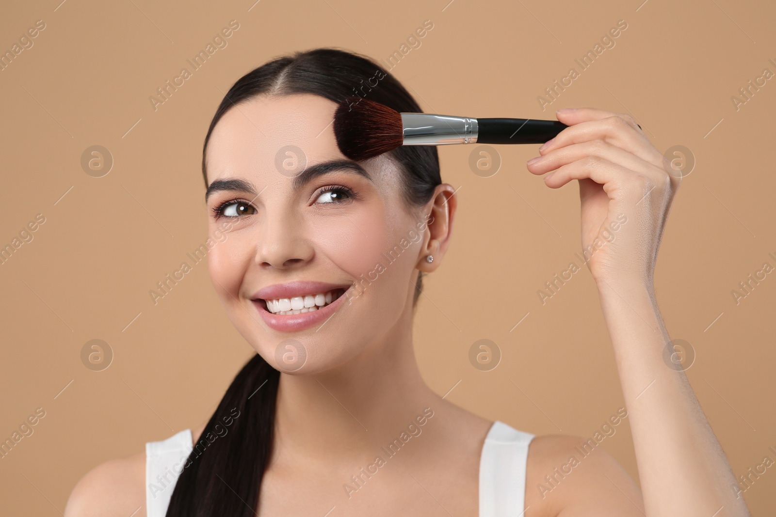 Photo of Beautiful woman applying makeup on light brown background