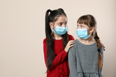 Little girls in medical masks on beige background, space for text. Virus protection