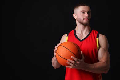 Photo of Athletic young man with basketball ball on black background. Space for text
