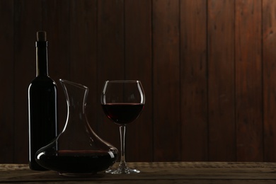 Bottle, decanter and glass with red wine on table against dark background